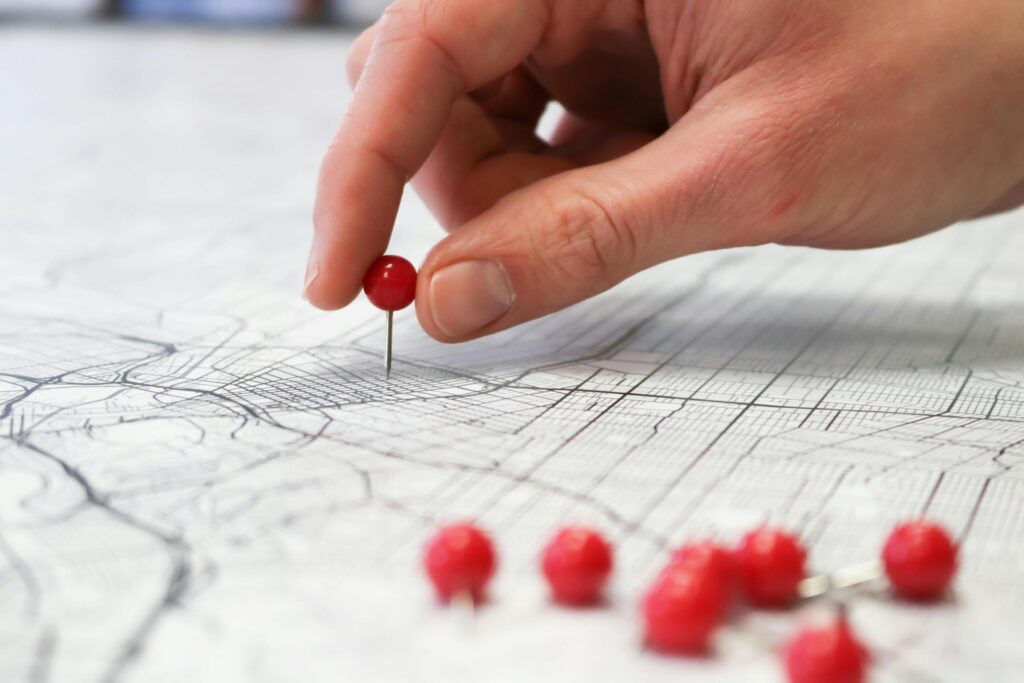 Close-up of a hand placing a red pin on a map indicating geographic location pinning.